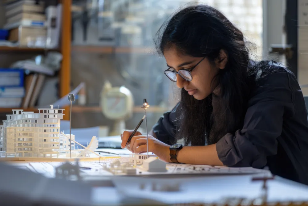 Design student sketching plans beside a scale architecture model at Raga Design Academy